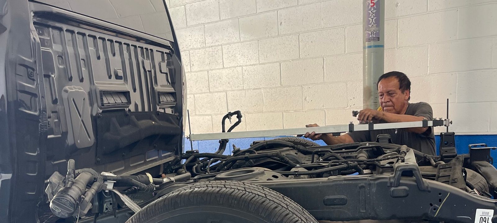 A technician holding a tram gauge across the frame rails of a stripped truck front end in the Northridge shop